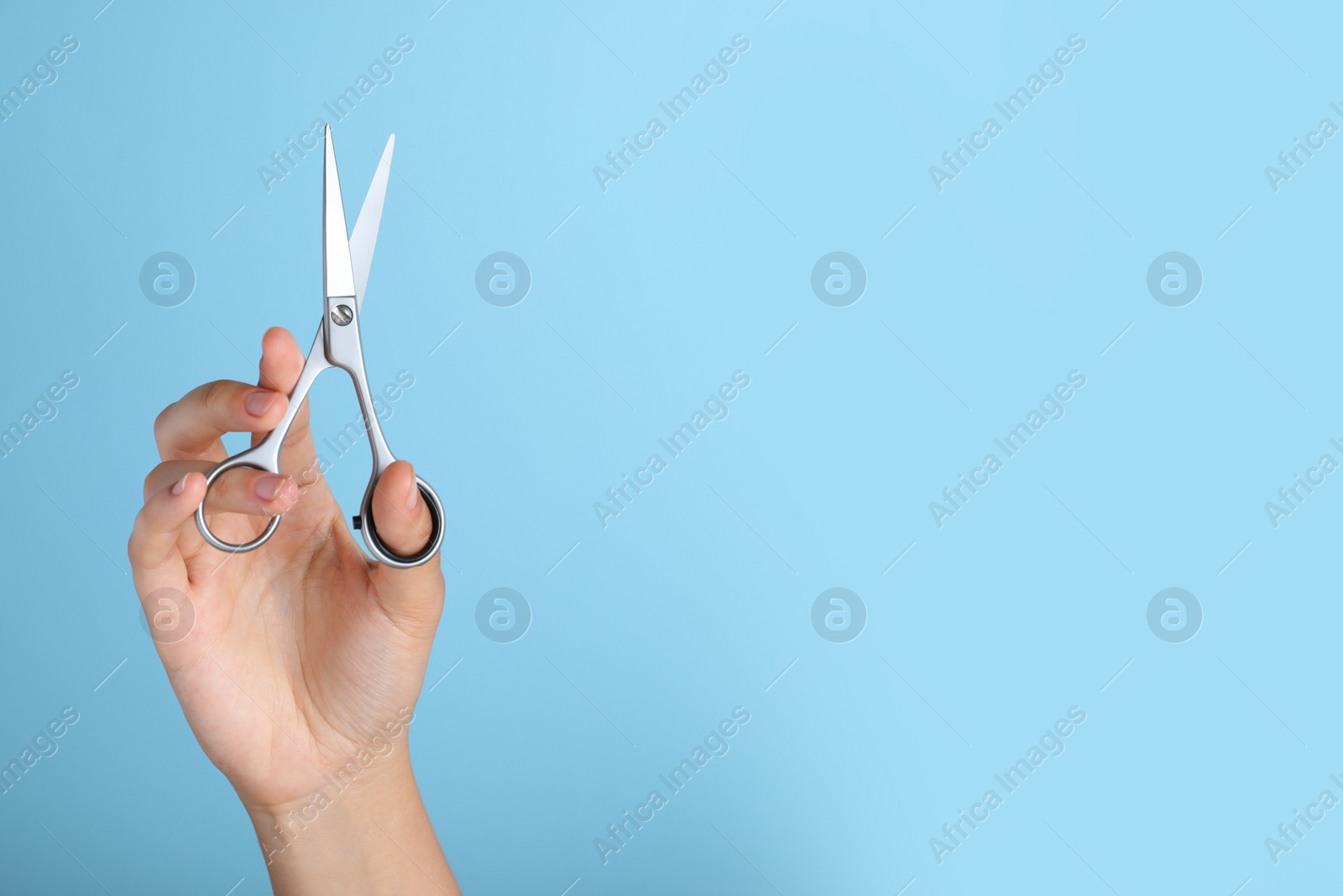 Photo of Hairdresser holding professional scissors and space for text on turquoise background, closeup. Haircut tool