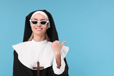 Photo of Happy woman in nun habit pointing at something against light blue background. Space for text