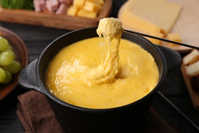 Dipping piece of ham into fondue pot with melted cheese on table, closeup