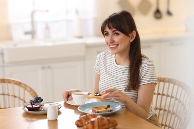 Smiling woman eating tasty breakfast at table indoors