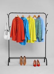 Rack with accessories and stylish clothes on wooden hangers against light grey background