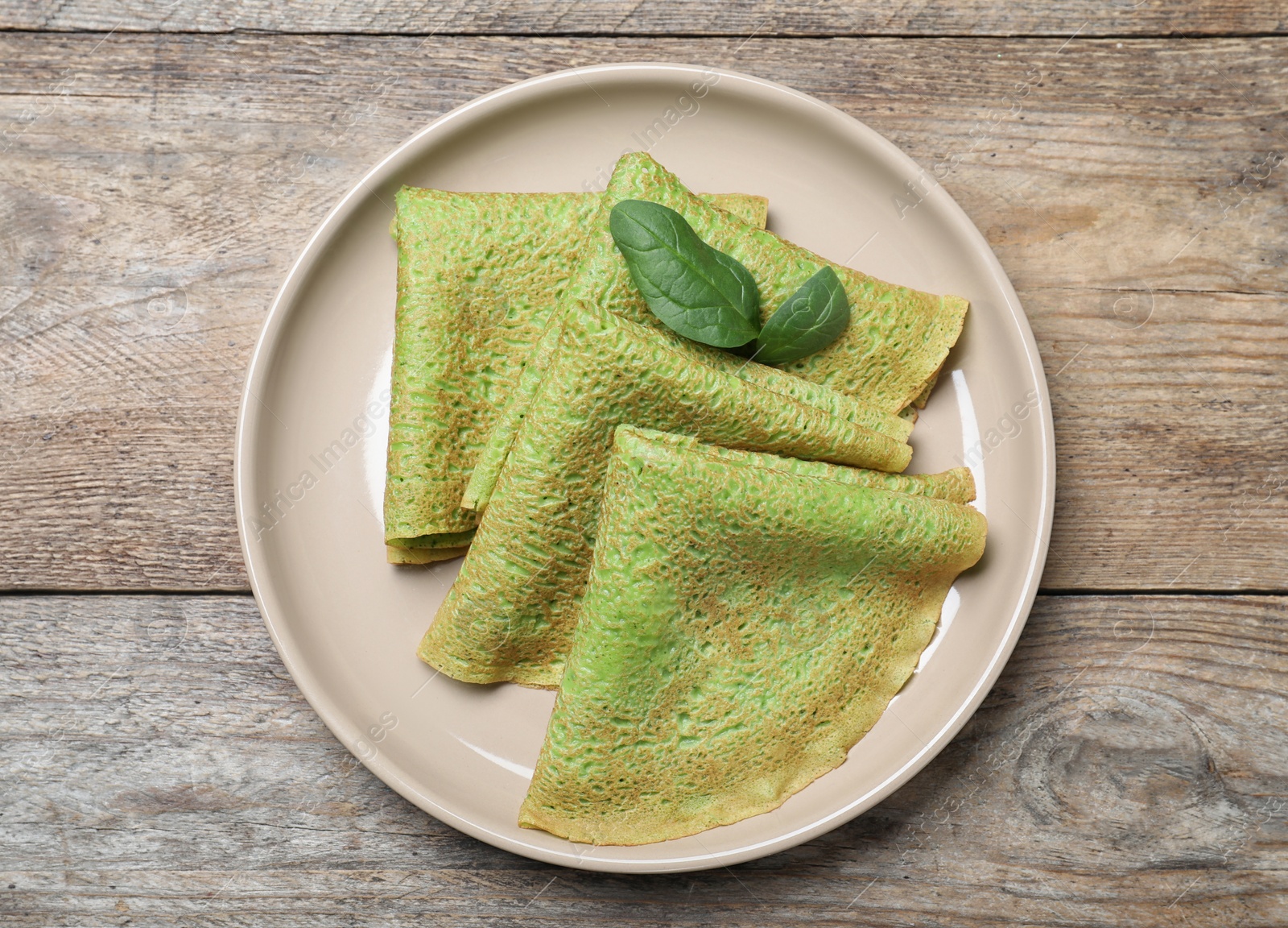 Photo of Delicious spinach crepes on wooden table, top view