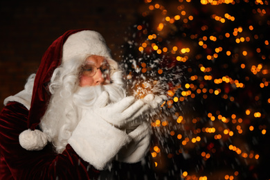 Photo of Santa Claus blowing snow against blurred lights. Christmas time