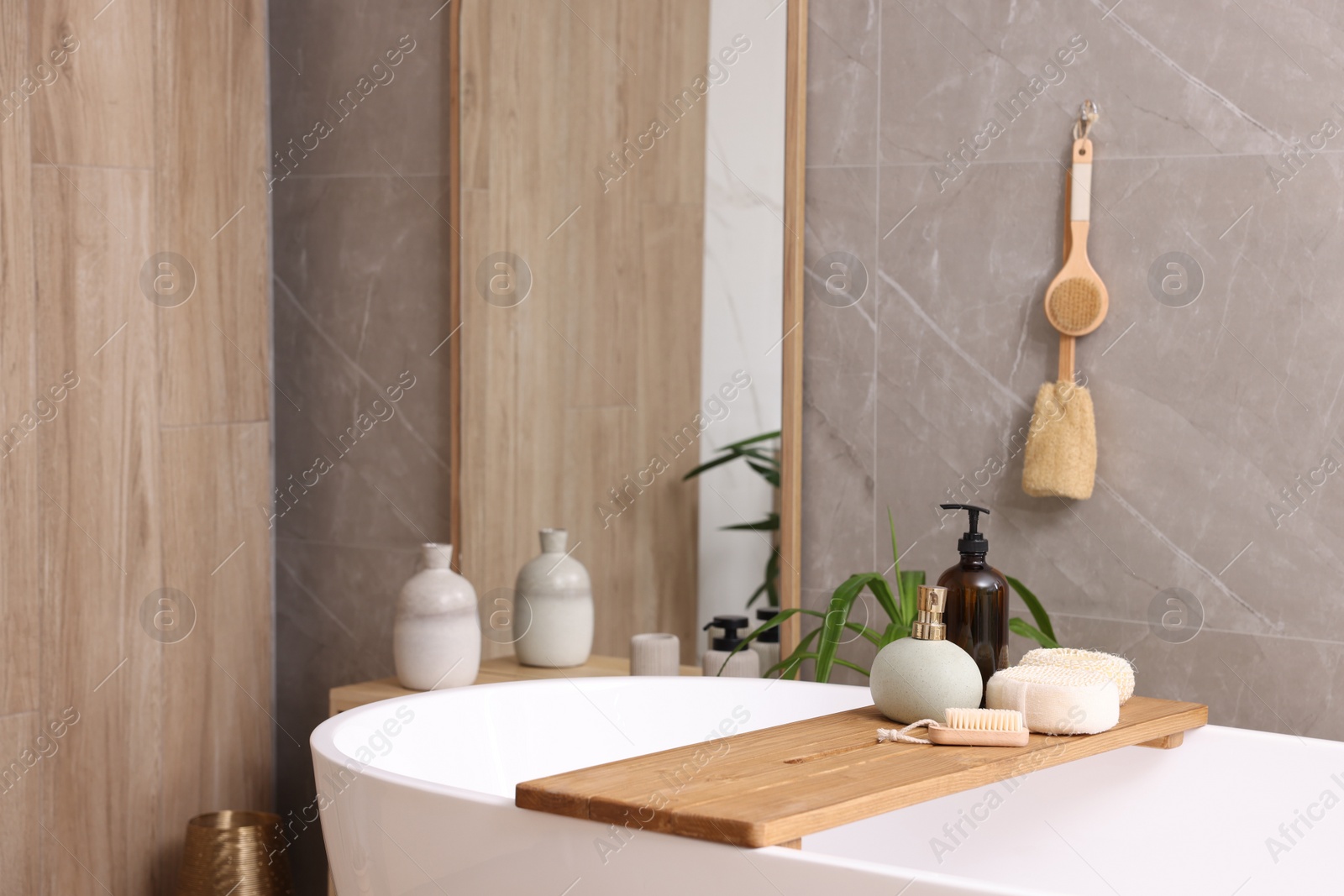 Photo of Modern ceramic bathtub, tray with toiletries and mirror indoors. Interior design