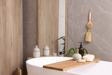 Modern ceramic bathtub, tray with toiletries and mirror indoors. Interior design