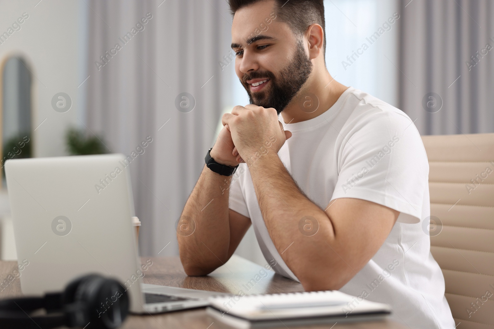 Photo of Young man watching webinar at table in room