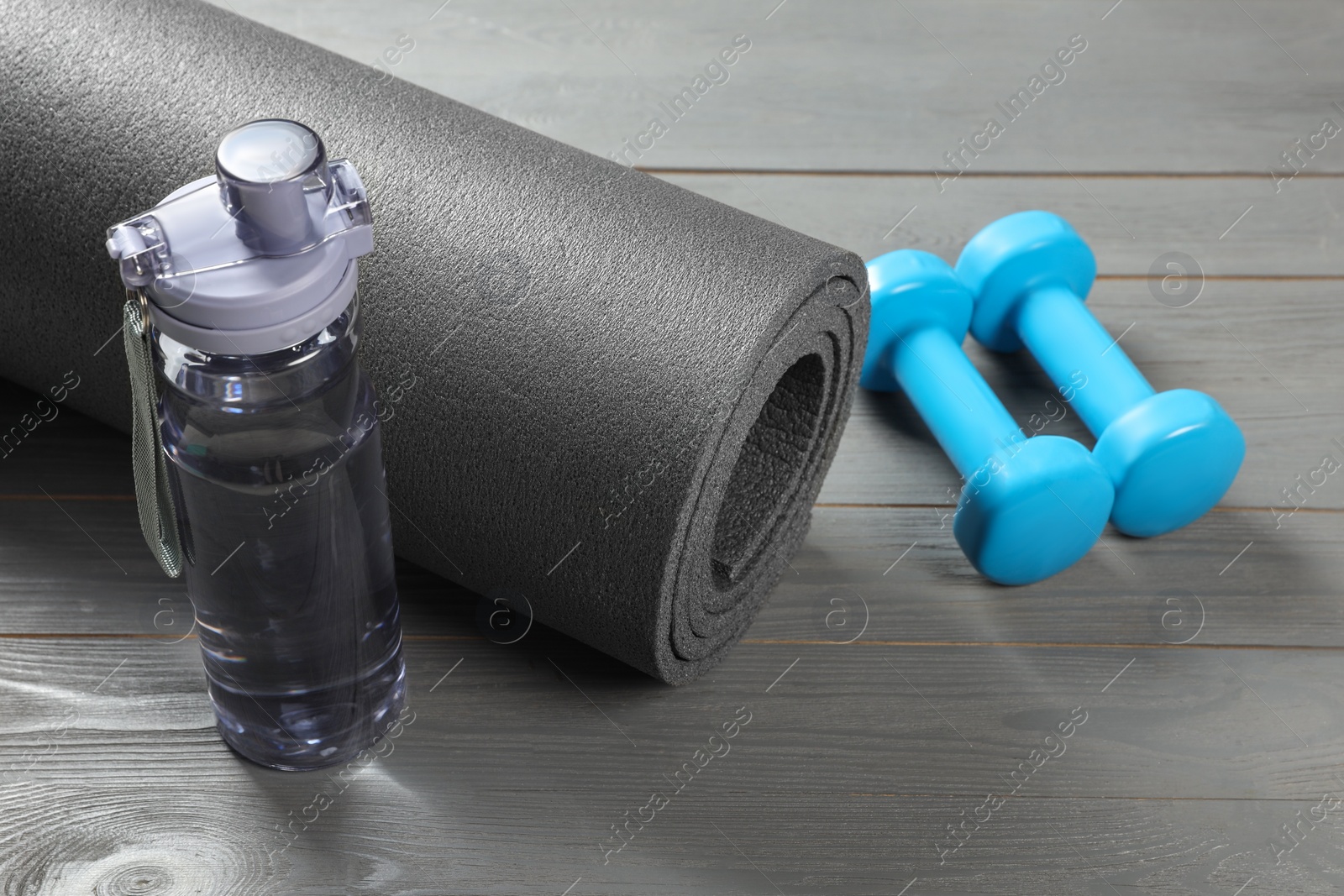 Photo of Yoga mat, bottle of water and dumbbells on grey wooden floor