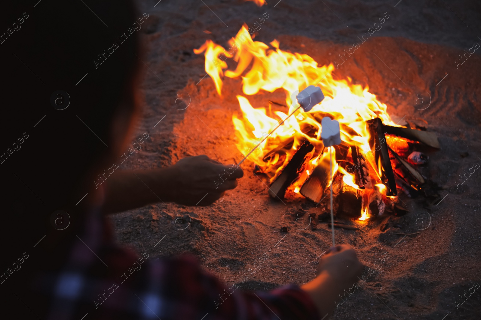 Photo of People roasting marshmallows over burning firewood on beach, closeup