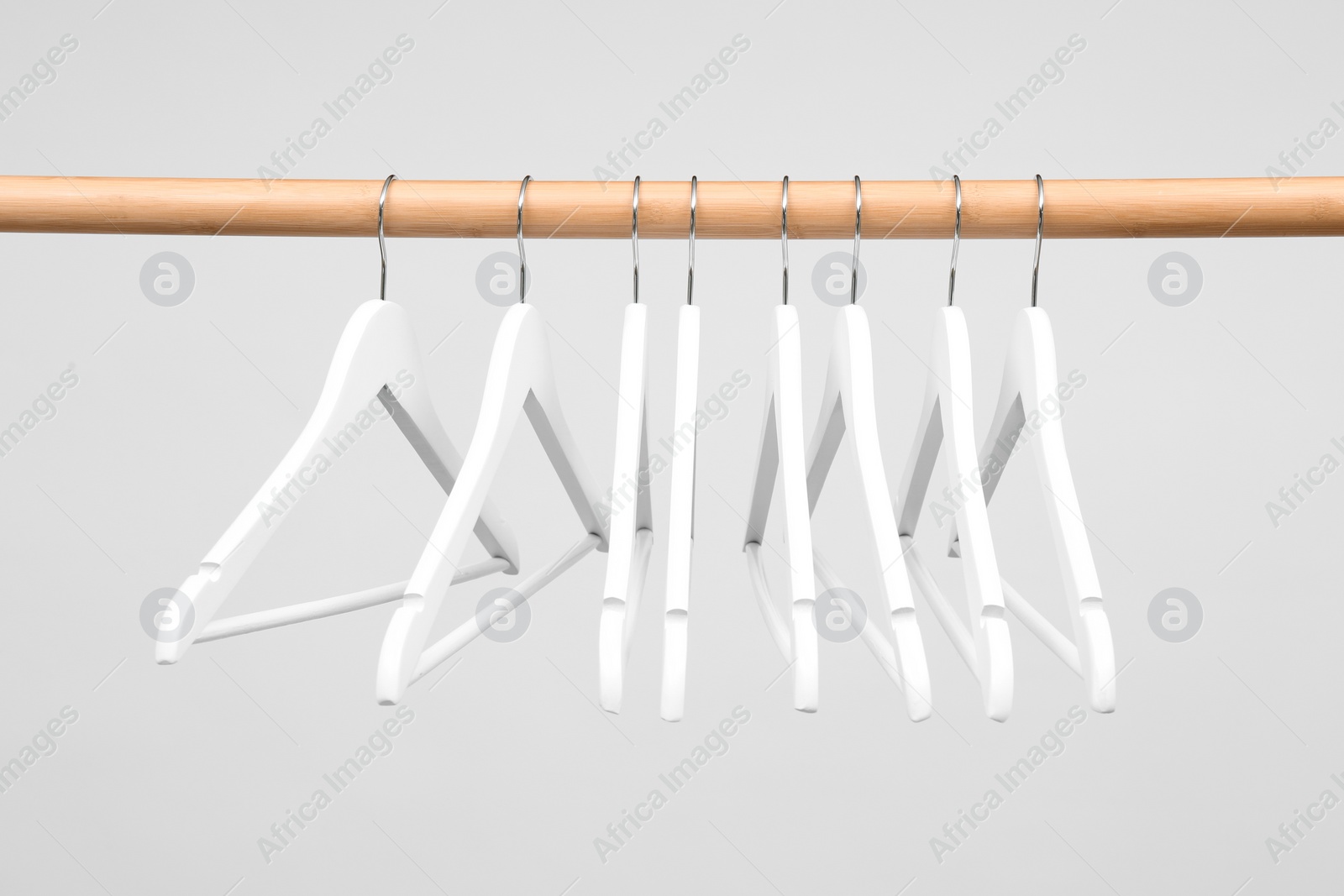 Photo of Empty clothes hangers on wooden rail against light background