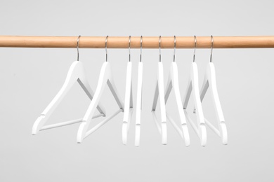 Photo of Empty clothes hangers on wooden rail against light background