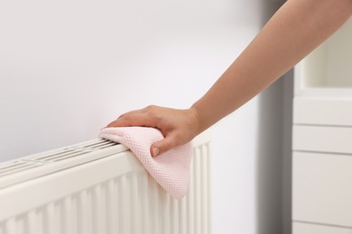 Photo of Woman cleaning radiator with rag indoors, closeup