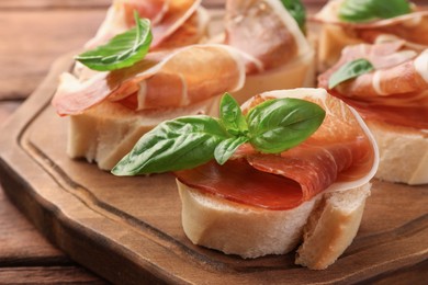 Board of tasty sandwiches with cured ham and basil leaves on table, closeup