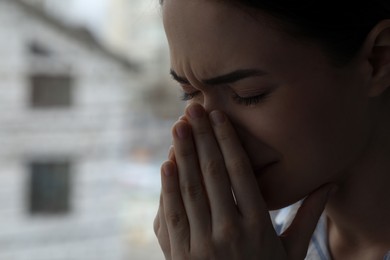 Photo of Sad young woman crying near window indoors, closeup with space for text. Loneliness concept