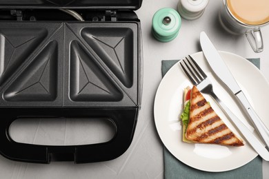 Modern grill maker and sandwich on light grey table, flat lay