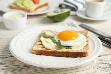 Photo of Slice of bread with fried egg, spread and arugula on white wooden table