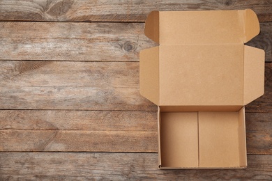 Photo of Open cardboard box on wooden background, top view. Space for text