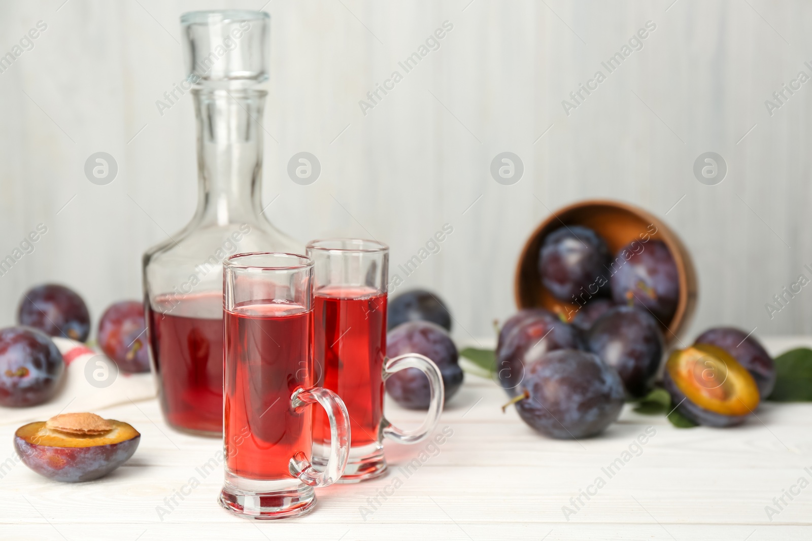 Photo of Delicious plum liquor and ripe fruits on white wooden table, space for text. Homemade strong alcoholic beverage