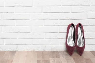 Photo of Stylish high heel shoes on floor near brick wall, space for text