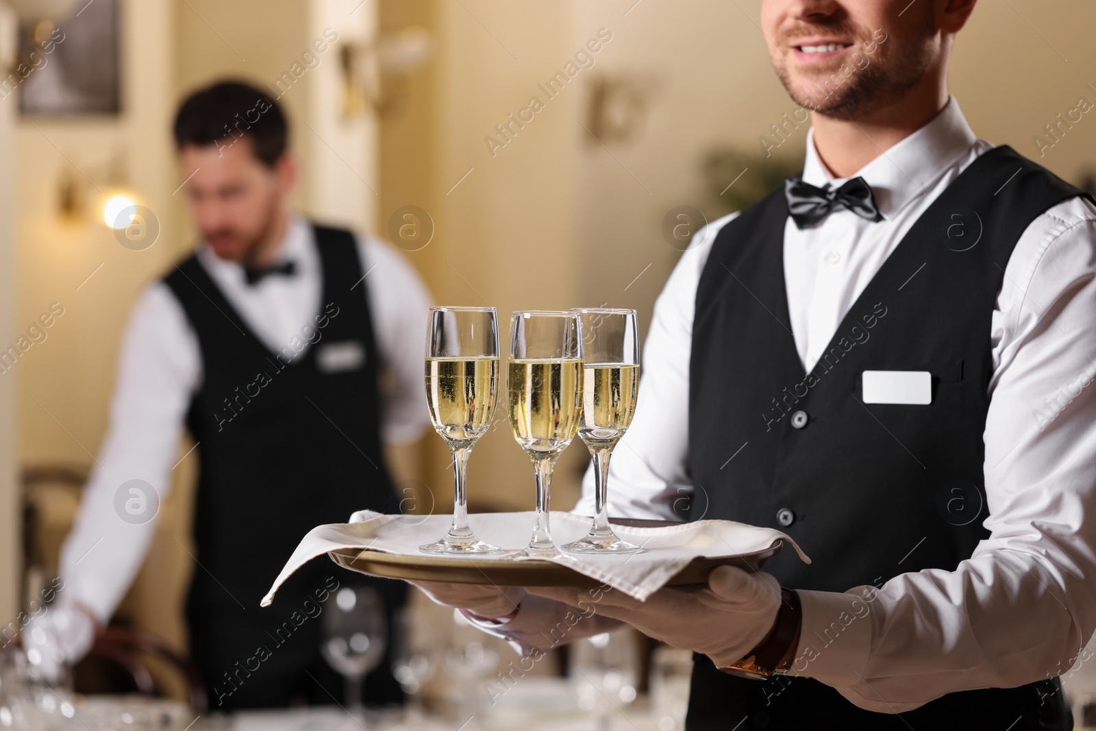 Photo of Butler holding tray with glasses of sparkling wine in restaurant, closeup