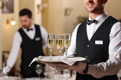 Photo of Butler holding tray with glasses of sparkling wine in restaurant, closeup