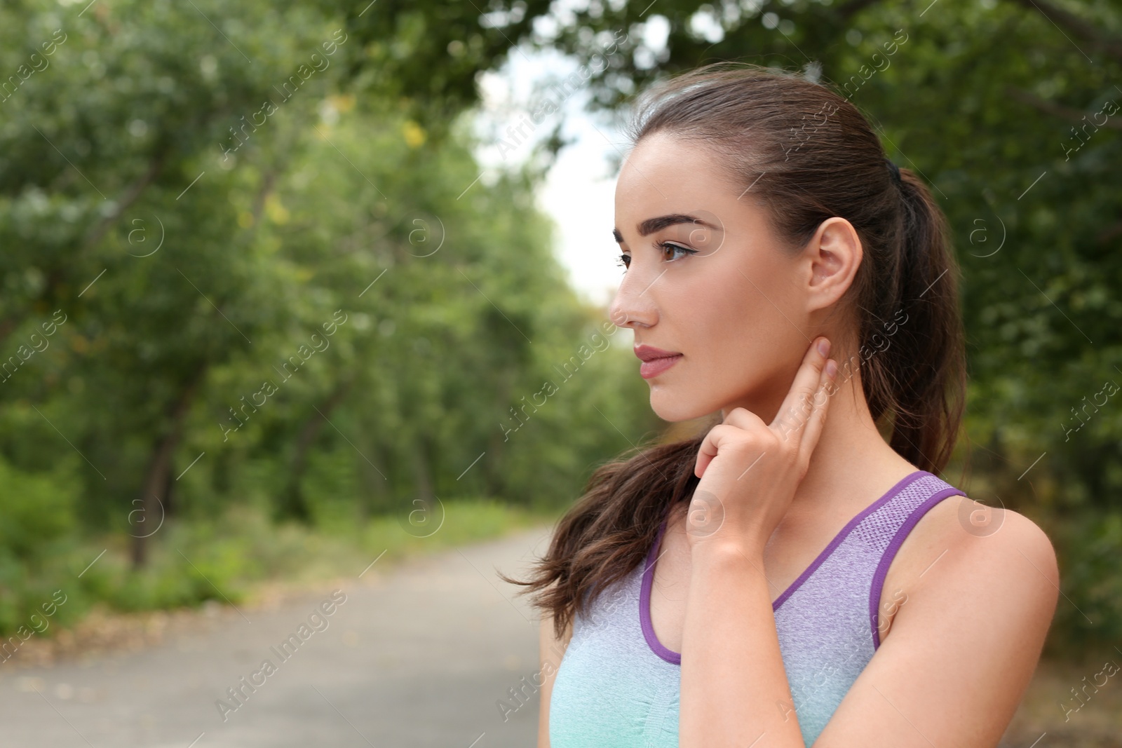 Photo of Young woman checking pulse after training in park. Space for text