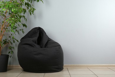 Black bean bag chair and houseplant near light grey wall in room. Space for text