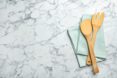 Wooden spatula, fork and napkin on marble background, top view with space for text