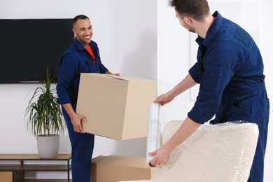 Photo of Male movers with armchair and cardboard box in new house