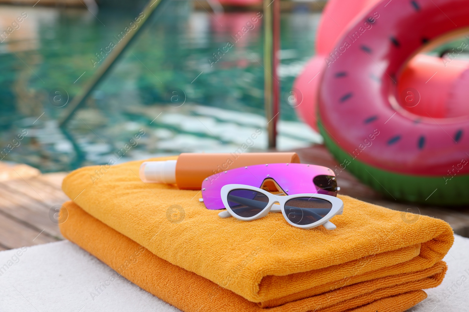 Photo of Beach towels, sunglasses and sunscreen on sunbed near outdoor swimming pool. Luxury resort