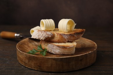 Photo of Tasty butter curls and slices of bread on wooden table, closeup