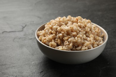 Photo of Tasty pearl barley porridge in bowl on dark textured table, closeup. Space for text