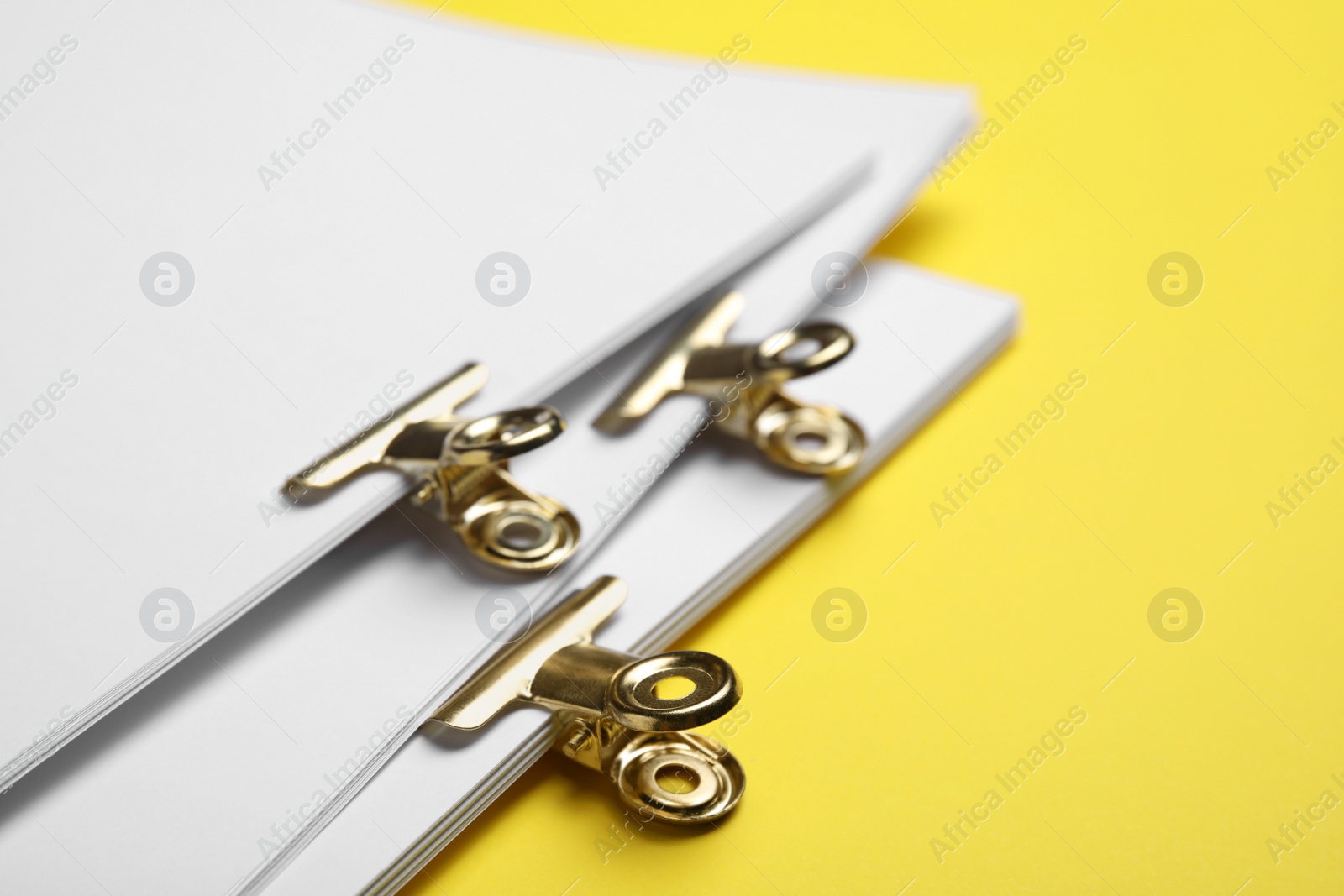 Photo of Sheets of paper with clips on yellow background, closeup