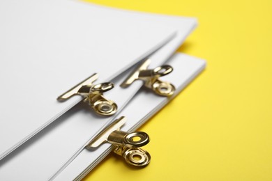 Photo of Sheets of paper with clips on yellow background, closeup