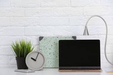 Photo of Modern workplace with laptop on table against brick wall. Mockup for design