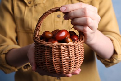 Photo of Woman holding wicker basket with fresh Ziziphus jujuba fruits on light background, closeup