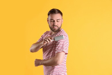 Photo of Young man cleaning clothes with lint roller on yellow background