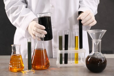 Woman holding beaker and test tube with black crude oil on dark background, closeup