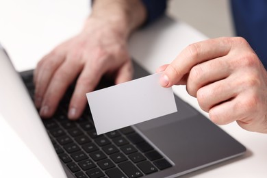 Man with laptop holding blank business card at white table, closeup