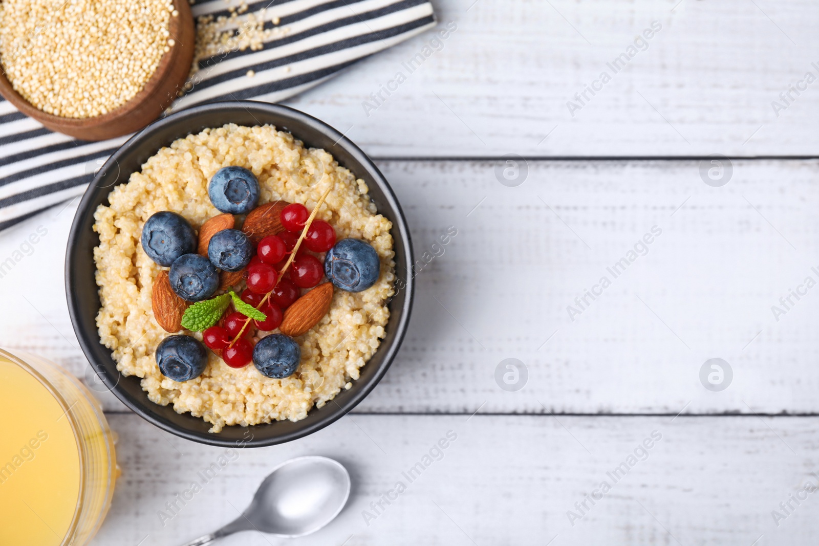 Photo of Bowl of delicious cooked quinoa with almonds, cranberries and blueberries on white wooden table, flat lay. Space for text