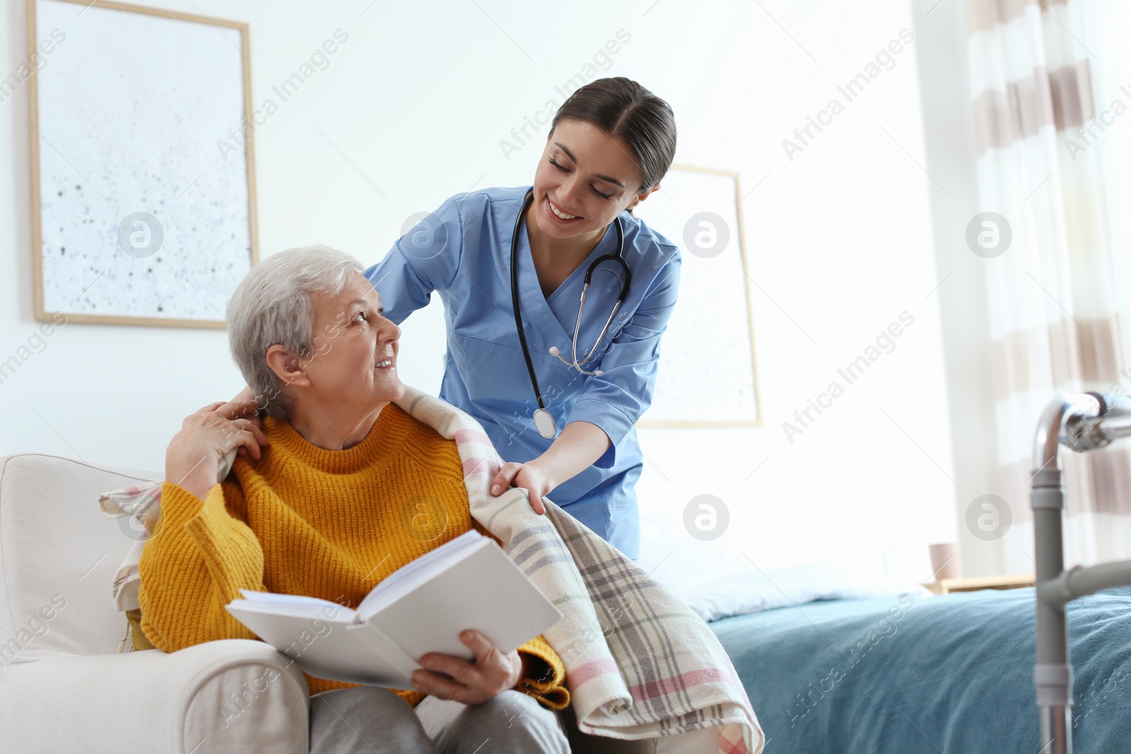 Photo of Care worker covering elderly woman with plaid in geriatric hospice