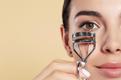 Photo of Beautiful young woman using eyelash curler on beige background, closeup. Space for text