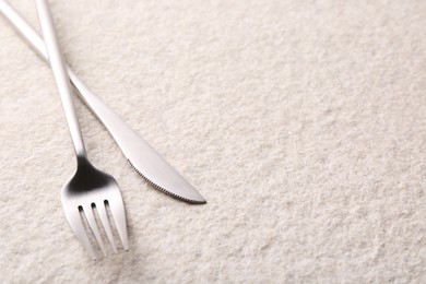 Photo of Stylish cutlery. Silver knife and fork on light textured table, space for text