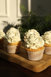 Photo of Tasty cupcakes with vanilla cream on wooden table, closeup