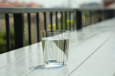 Photo of Glass of fresh water on white wooden table outdoors