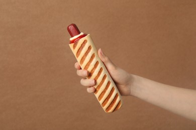 Photo of Woman holding delicious french hot dog on brown background, closeup