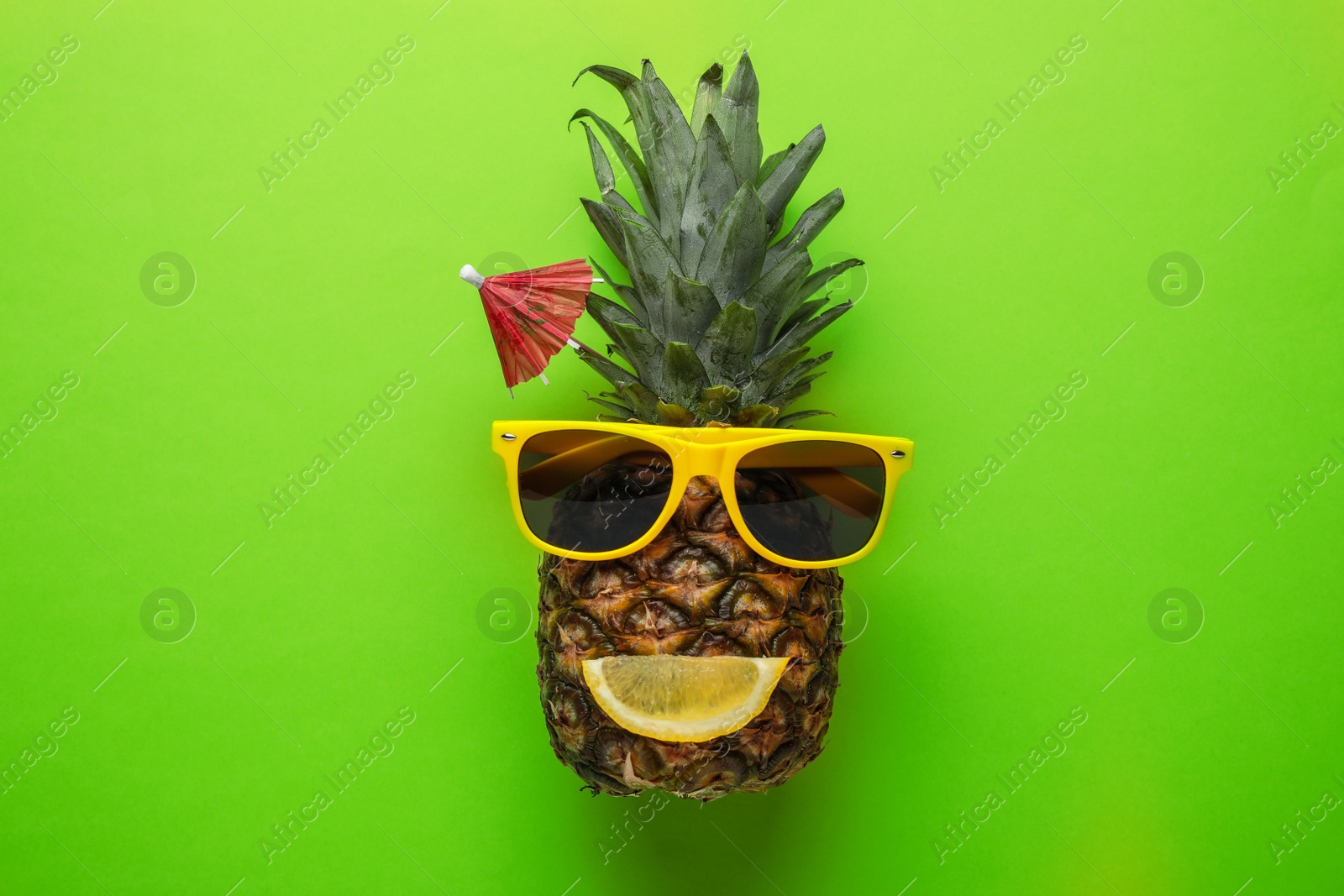 Photo of Funny face made of pineapple, sunglasses and citrus slice with cocktail umbrella on color background, top view