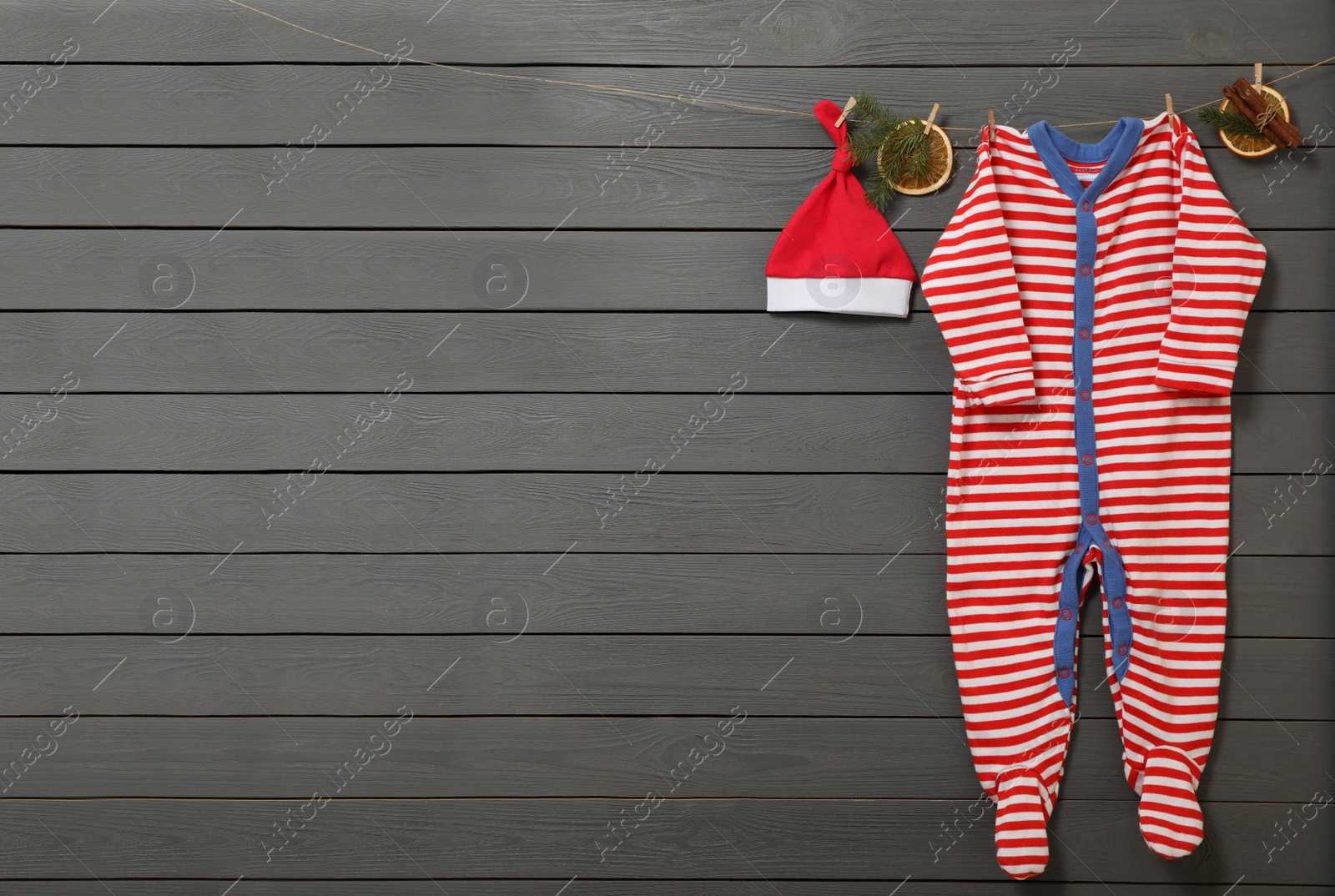 Photo of Cute Christmas baby clothes and decorations hanging on grey wooden wall. Space for text