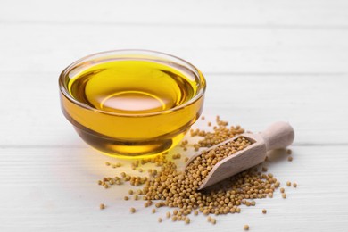 Photo of Bowl of natural oil and scoop with mustard seeds on white wooden table