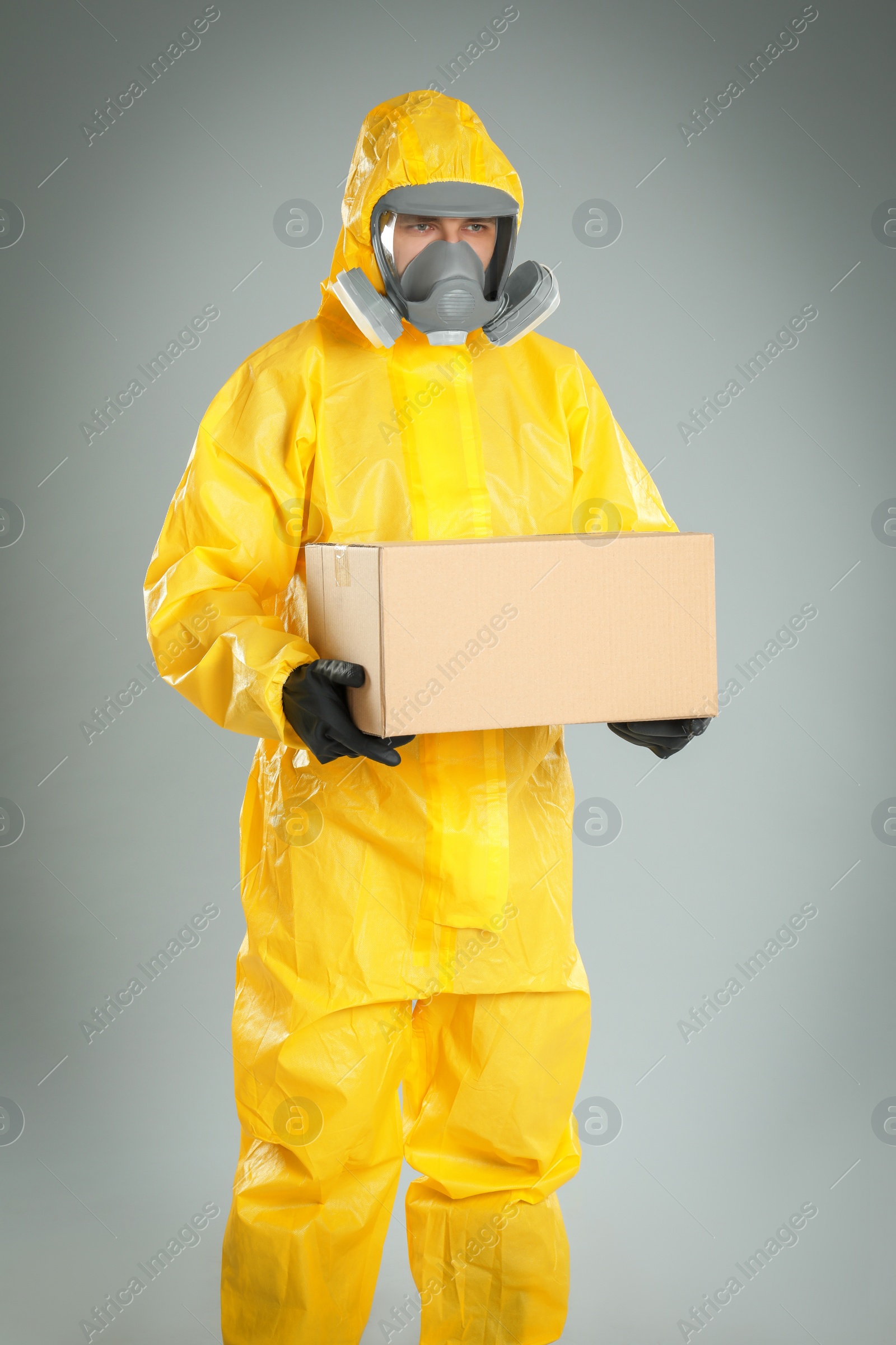 Photo of Man wearing chemical protective suit with cardboard box on light grey background. Prevention of virus spread