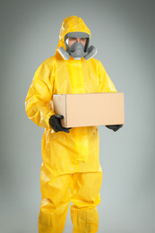 Photo of Man wearing chemical protective suit with cardboard box on light grey background. Prevention of virus spread